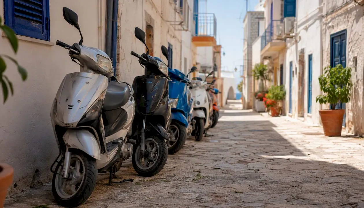 Een rij scooters staat geparkeerd langs een zonovergoten straat op een Mediterraan eiland.